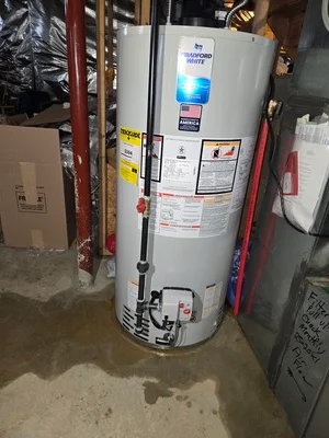 Installed gas water heater with blue control panel, copper connections, and safety equipment in utility room