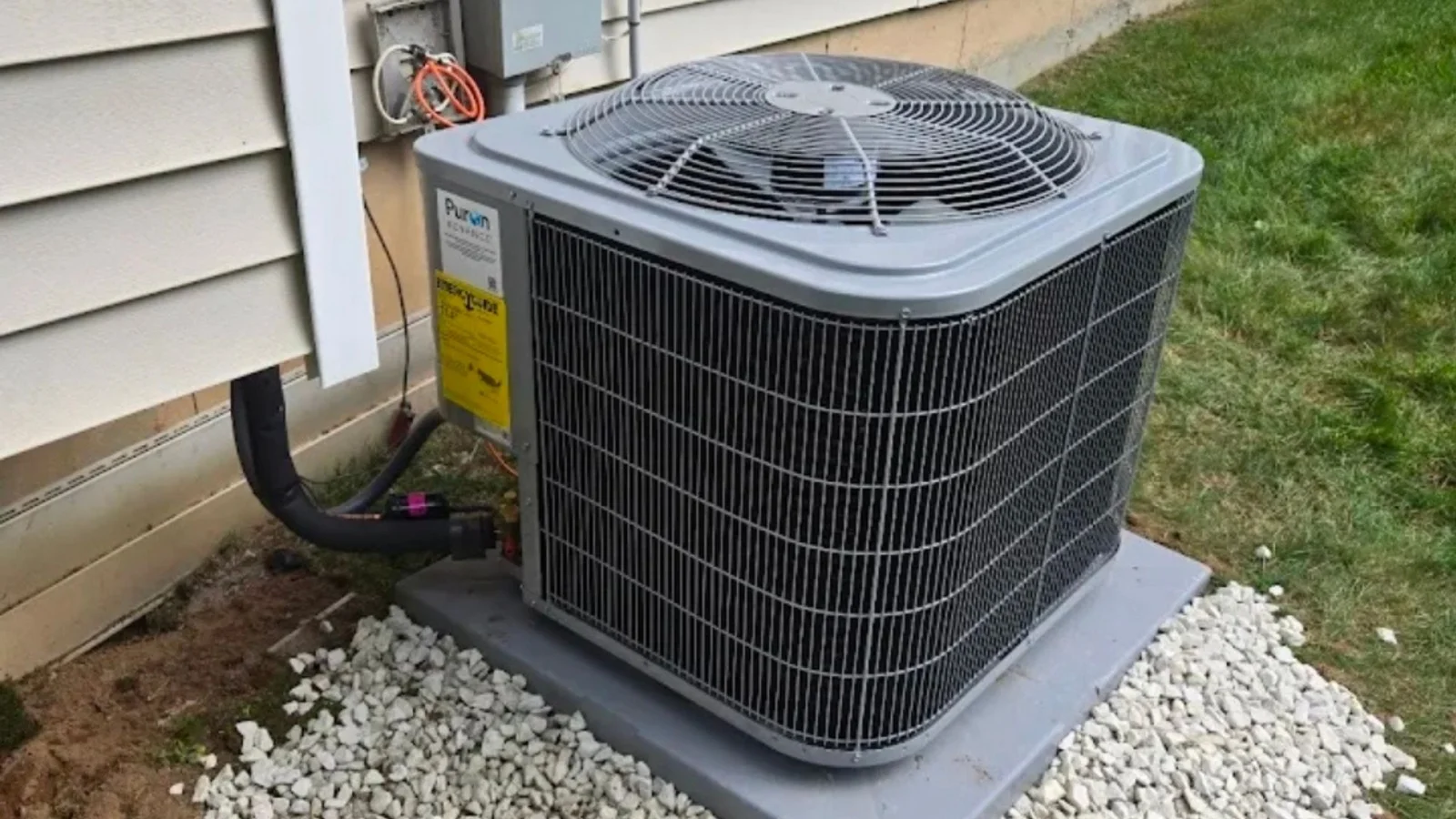 Installed air conditioning condenser unit on concrete pad with white stone base and refrigerant lines
