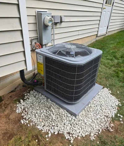 AC condenser unit on gravel pad with refrigerant lines and wall-mounted disconnect switch