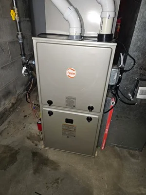 Stacked dual-stage gas furnace with white casing, ductwork, and gas connections in basement